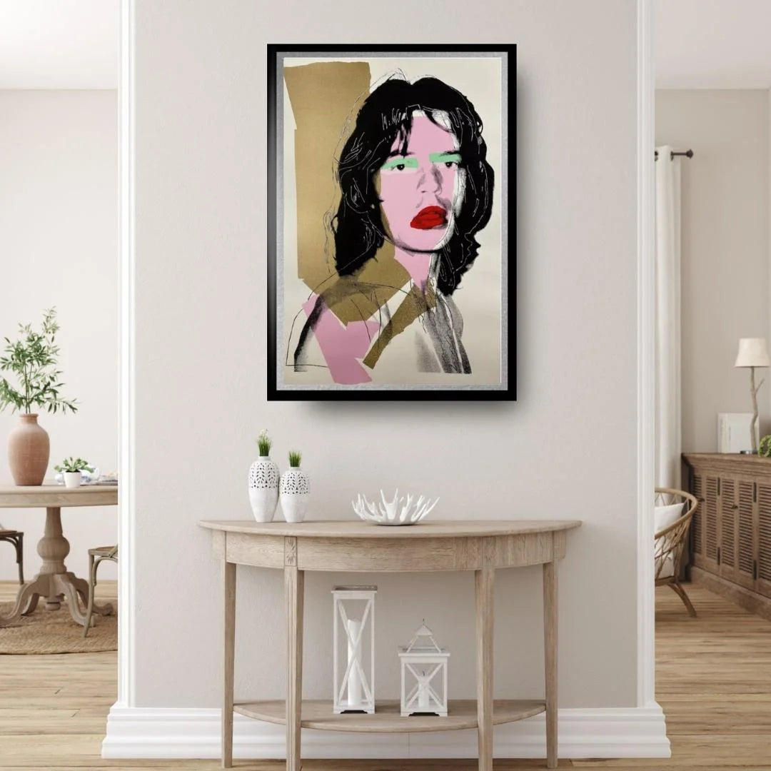 Framed artwork of a stylized portrait on a wall in a room with a table and decor items.