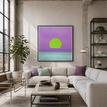 A framed abstract art print featuring a bright green circle against a purple and teal gradient background, displayed on a concrete wall above a modern light gray sectional sofa in a styled living room.
