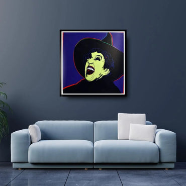 Framed artwork of a witch's face on a dark wall above a light blue sofa.