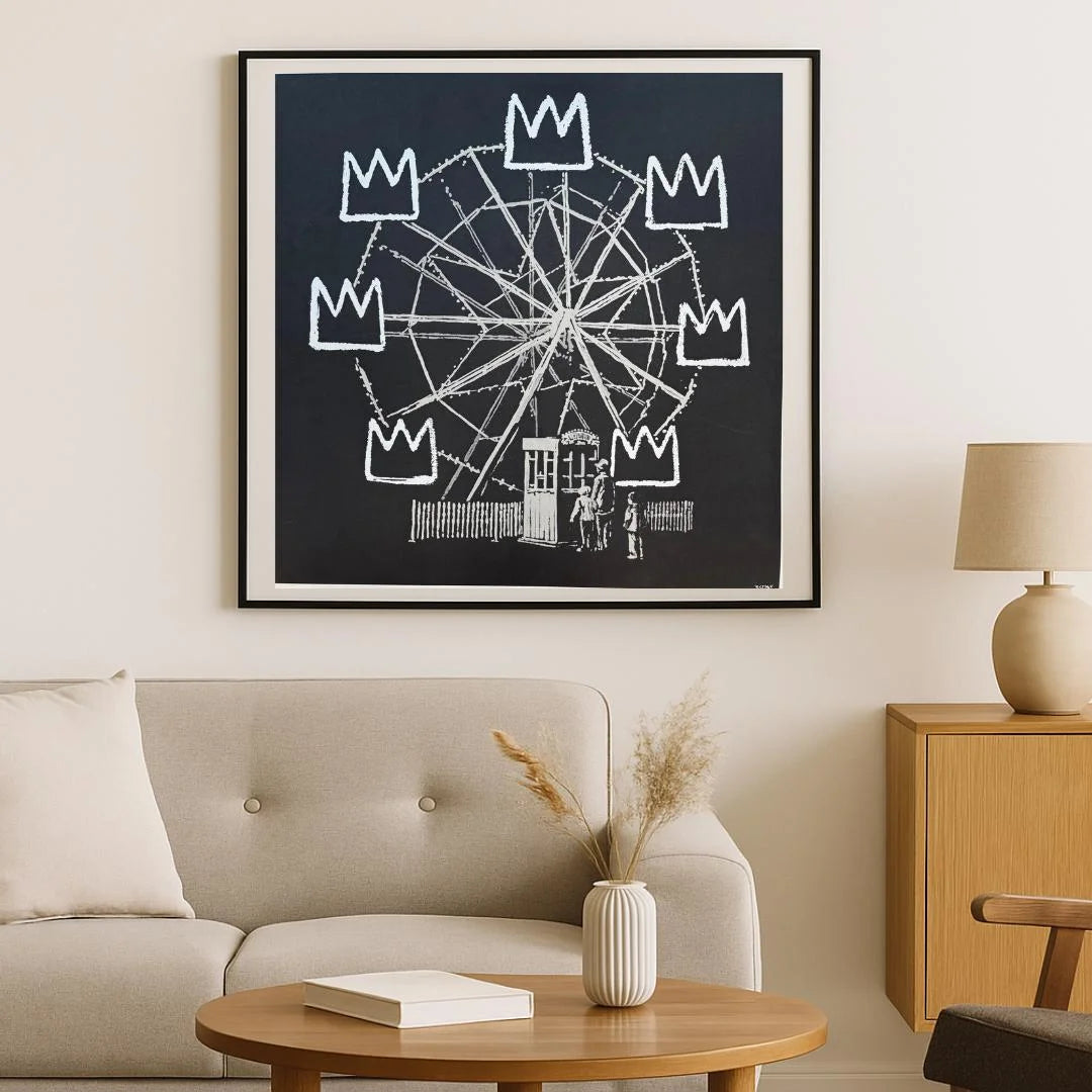 Framed artwork of a Ferris wheel with crowns above it in a living room . setting. BANKSY BANKSQUAIT