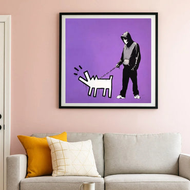 Framed Banksy artwork of a person walking a dog on a purple background above a sofa with colorful cushions.