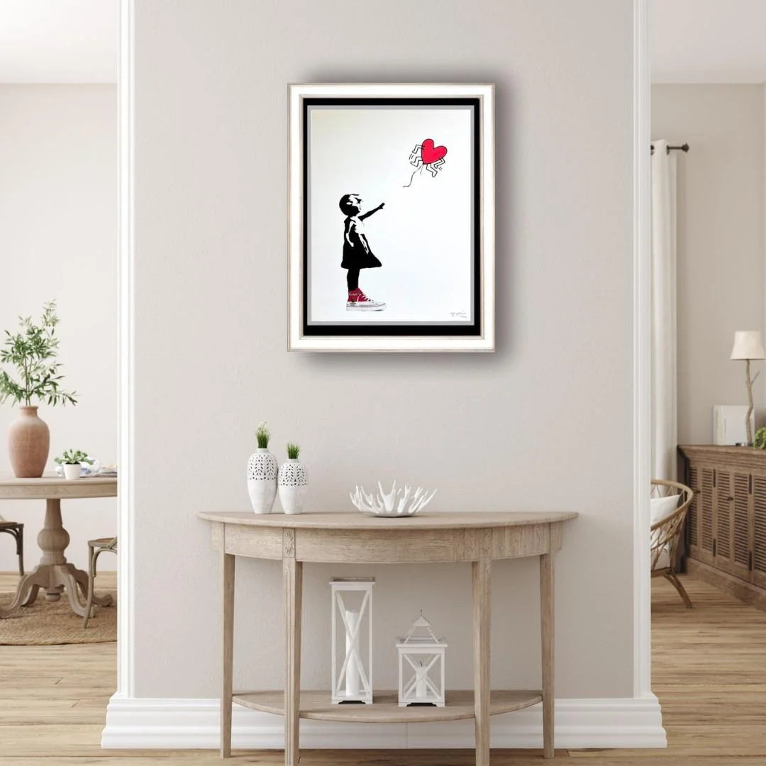 Framed artwork of a girl with a red balloon on a wall above a wooden table.