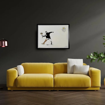 Yellow sofa in a room with a dark wall, framed artwork, and a plant.