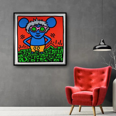 Framed colorful artwork on a gray wall with a red armchair below.