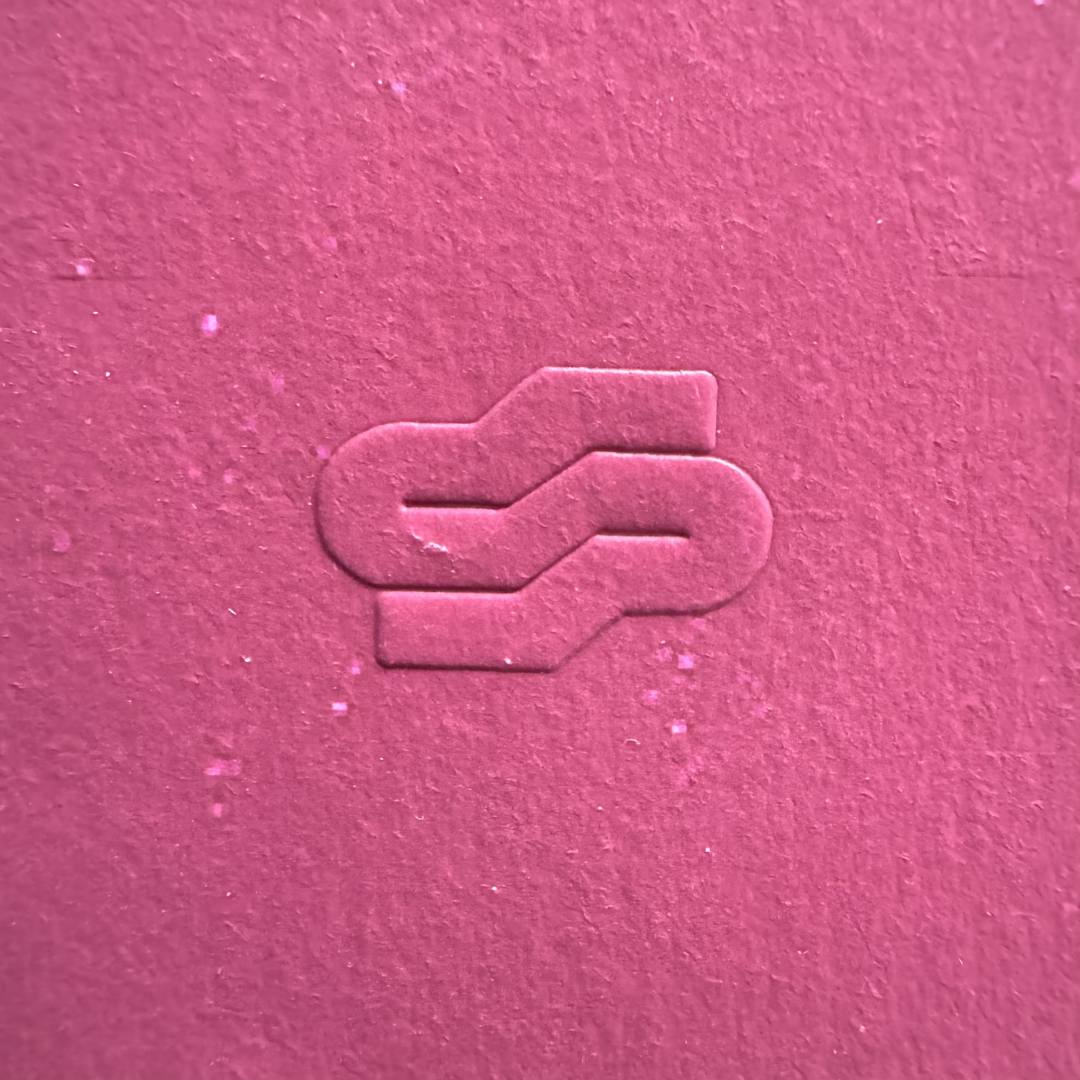 Textured pink surface with a logo or symbol embossed in the center.