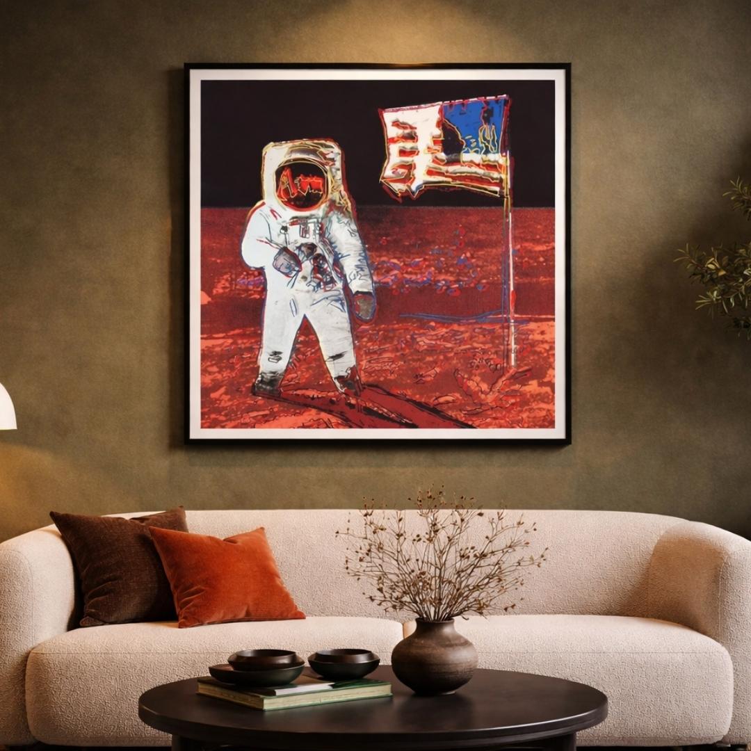 Framed artwork of an astronaut on the moon above a beige sofa with decorative items.