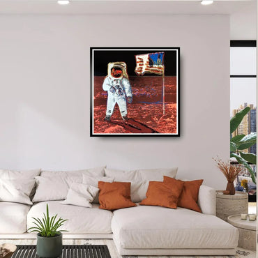 Framed artwork of Andy Warhol's Moonwalk, an astronaut on the moon,  above a white sofa with orange and white pillows.
