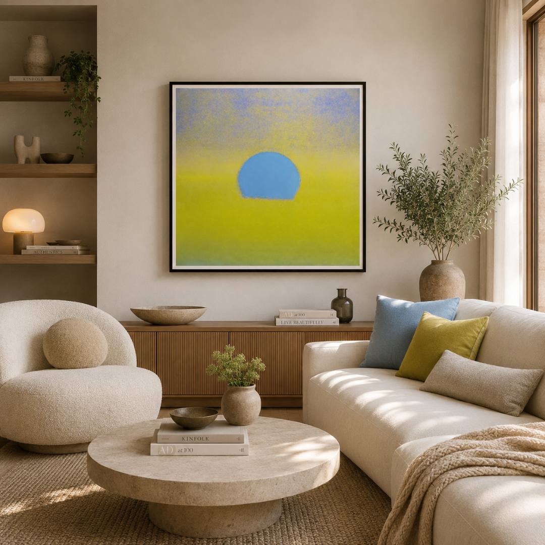 A framed abstract wall art print hangs above a wooden console in a styled living room. The artwork features a soft blue half-circle centered against a yellow-to-light-blue gradient background.