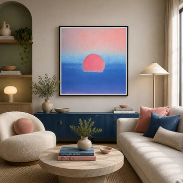 A framed abstract wall art print featuring a pink sun over a blue gradient sky, displayed in a modern living room setting above a blue sideboard.